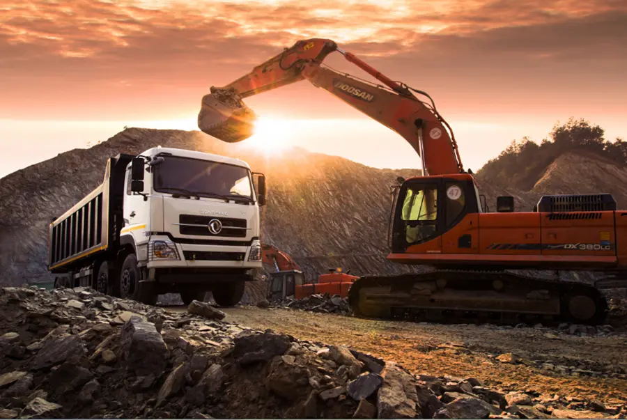 Construction machinery: a white dump truck and Doosan DX380LC excavator working together on a rocky terrain under a dramatic sunset sky