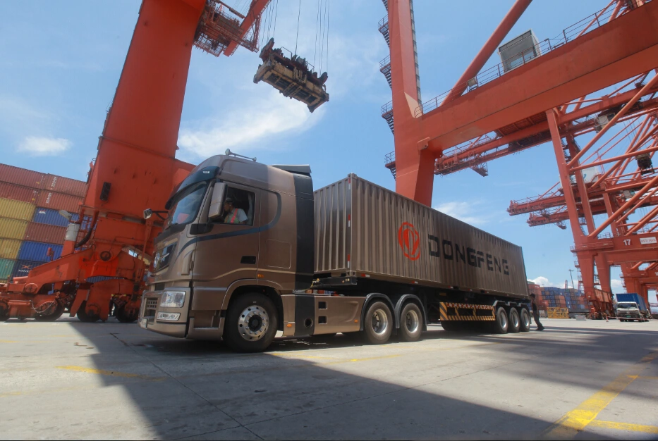 Dongfeng heavy-duty truck with container trailer operating at a busy port, engineered for reliable long-haul logistics, containerized freight transport, and efficient global supply chain operations.